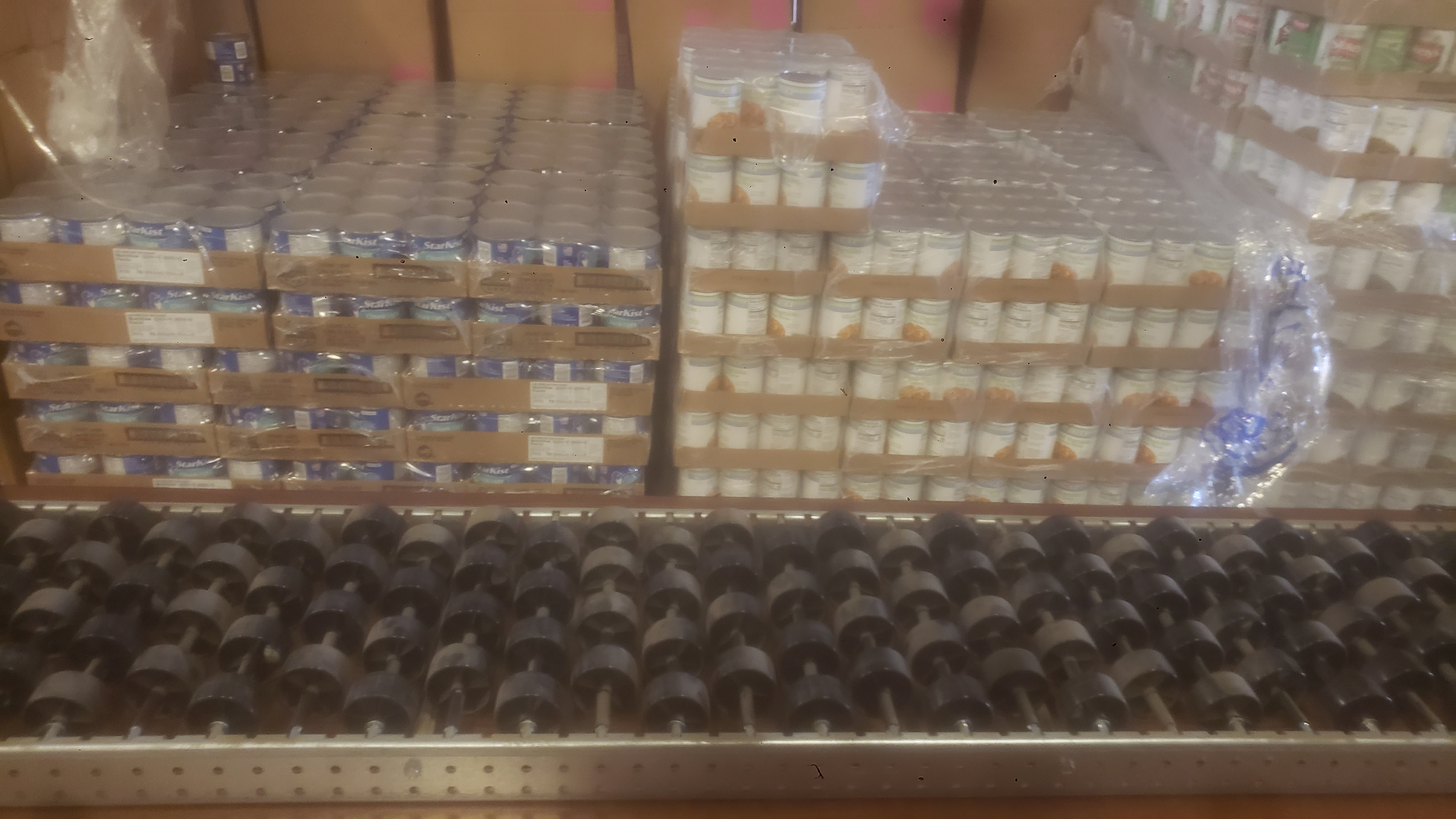 Conveyor belt on a table with pallets of canned foods behind it.